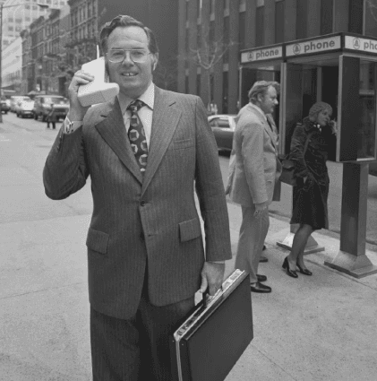 A man in the 80s with a cell phone appropriate for that era